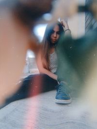 Young woman sitting on mirror against blurred background