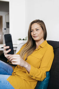 Young woman using mobile phone while sitting on sofa at home