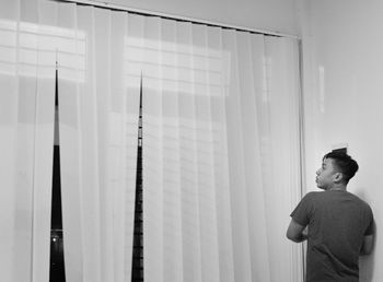 Young man standing by window blinds at home