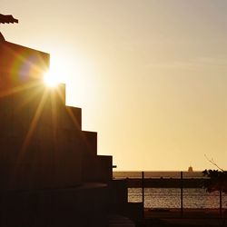 Silhouette building by sea against clear sky during sunset