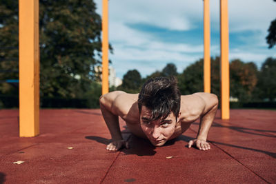 Young shirtless man bodybuilder doing push-ups on a red rubber ground during his workout