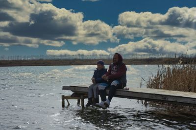 Couple sitting on shore against sky