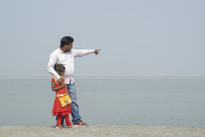 Full length of father pointing at sea while standing with daughter
