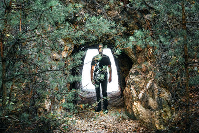 Man standing in cave by pine trees