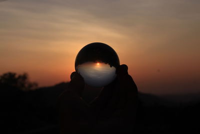 Silhouette person holding camera against sky during sunset