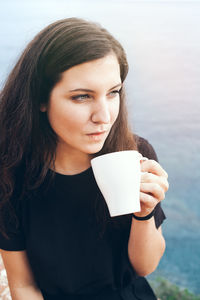 Beautiful young woman drinking coffee while sitting against blurred background