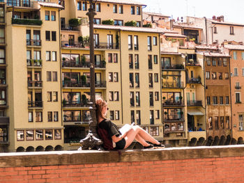 Side view of a woman sitting against buildings