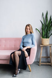 Portrait of young woman sitting on chair against wall