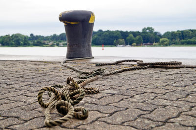 Close-up of rope on pier with mooring ring by lake against sky