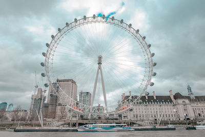 Ferris wheel in city against cloudy sky