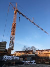 Low angle view of crane by building against blue sky