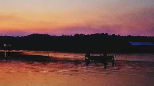 Silhouette trees on shore against sky during sunset