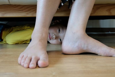 Portrait of girl looking through person leg while lying on hardwood floor