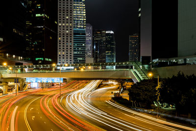 Light trails on road by illuminated buildings in city at night