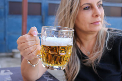 Mature woman holding beer glass sitting outdoors