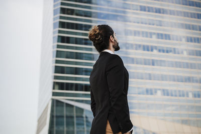 Businessman with hands in pockets looking away while standing against building