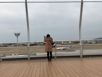 Rear view of woman with umbrella standing on railing