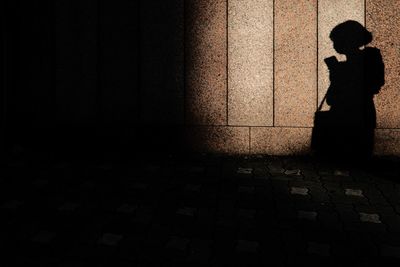 Silhouette girl standing on sidewalk against wall