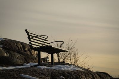 Low angle view of empty bench on rock against sky during sunset