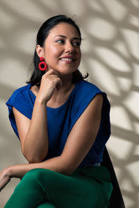 Portrait of a smiling young woman sitting against wall