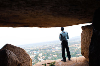 Rear view of man standing on rock against cityscape