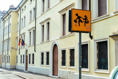 Low angle view of school crossing sign against buildings