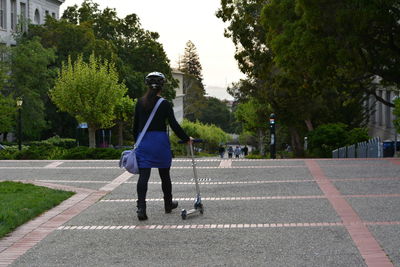 Rear view of woman with push scooter on footpath