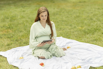 Young pretty pregnant woman holding, reading something on tablet,gadget,resting in park,sitting