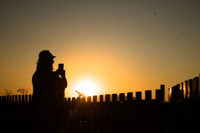 Silhouette woman photographing against orange sky