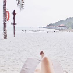 Low section of woman relaxing on lounge chair at sandy beach