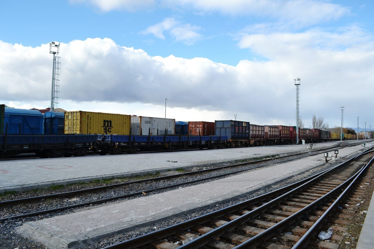 railroad track, rail transportation, transportation, sky, building exterior, railroad station platform, public transportation, railroad station, built structure, architecture, train - vehicle, cloud - sky, the way forward, mode of transport, railway track, cloud, cloudy, diminishing perspective, weather, electricity pylon