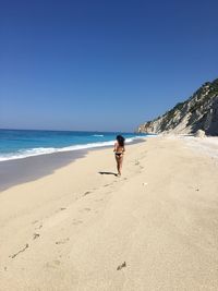 Full length of woman running at beach against clear sky