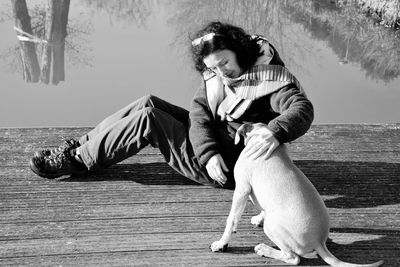 Side view of woman stroking dog while sitting on pier by lake