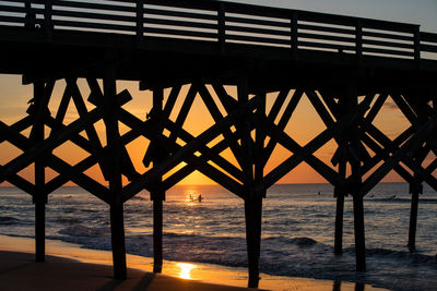 Silhouette bridge over sea against sky during sunset