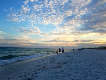 People walking on beach against sky during sunset