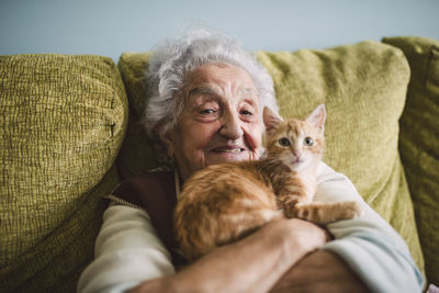 Portrait of happy senior woman cuddling with her cat on the couch