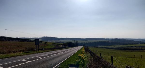 Empty road amidst field against sky