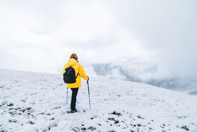 Back view of anonymous hiker with trekking poles walking on snowy ground in pyrenees mountains in andorra