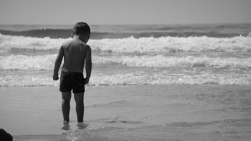 Rear view of shirtless boy wading in sea