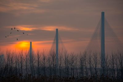 View of suspension bridge against cloudy sky during sunset