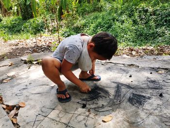 High angle view of boy drawing with chalk on footpath