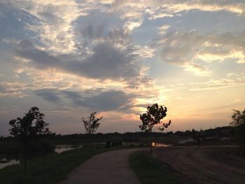 Road by trees on field against sky at sunset