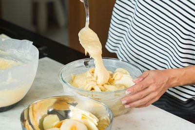 Woman putting dough in the baking dish while cooking apple pie in the modern kitchen