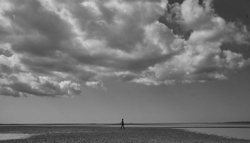 Scenic view of sea with person walking at beach against sky