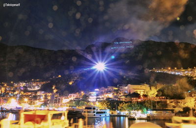 Illuminated buildings by sea against sky at night