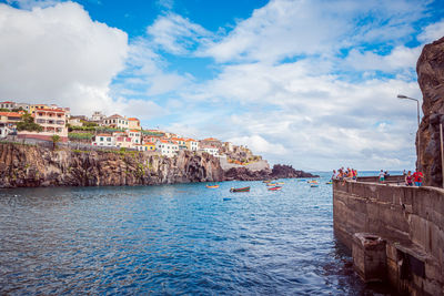 Buildings by sea against cloudy sky