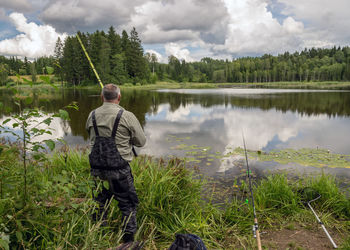  fisherman on the lake shore, lake grass in the foreground, traditional summer nature