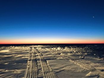 Tire tracks on sand against clear blue sky