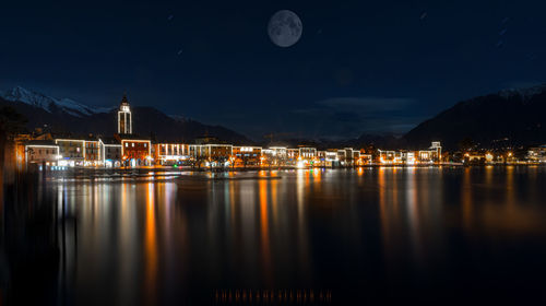 Illuminated buildings by lake against sky at night