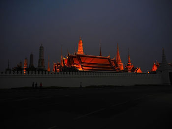 Empty road by illuminated wat phra kaew against clear sky at dusk